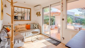 A modern living room with a sofa, a coat rack, a dining area with a table and chairs, and a sliding glass door leading to an outdoor patio. - Les Coteaux de la Nartelle by Interhome (Sainte Maxime)