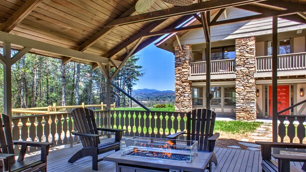 Una terraza exterior con sillas Adirondack, una chimenea y un pilar de piedra.