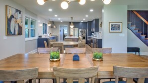 Un comedor espacioso con una mesa y sillas de madera, un candelabro y una cocina al fondo.