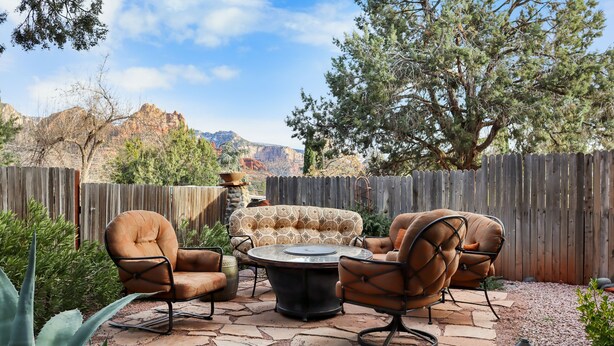 An outdoor patio with a stone table and leather chairs, surrounded by a wooden fence and a view of mountains. - Uptown Luxury Sedona House @ The Matterhorn Inn (Sedona)