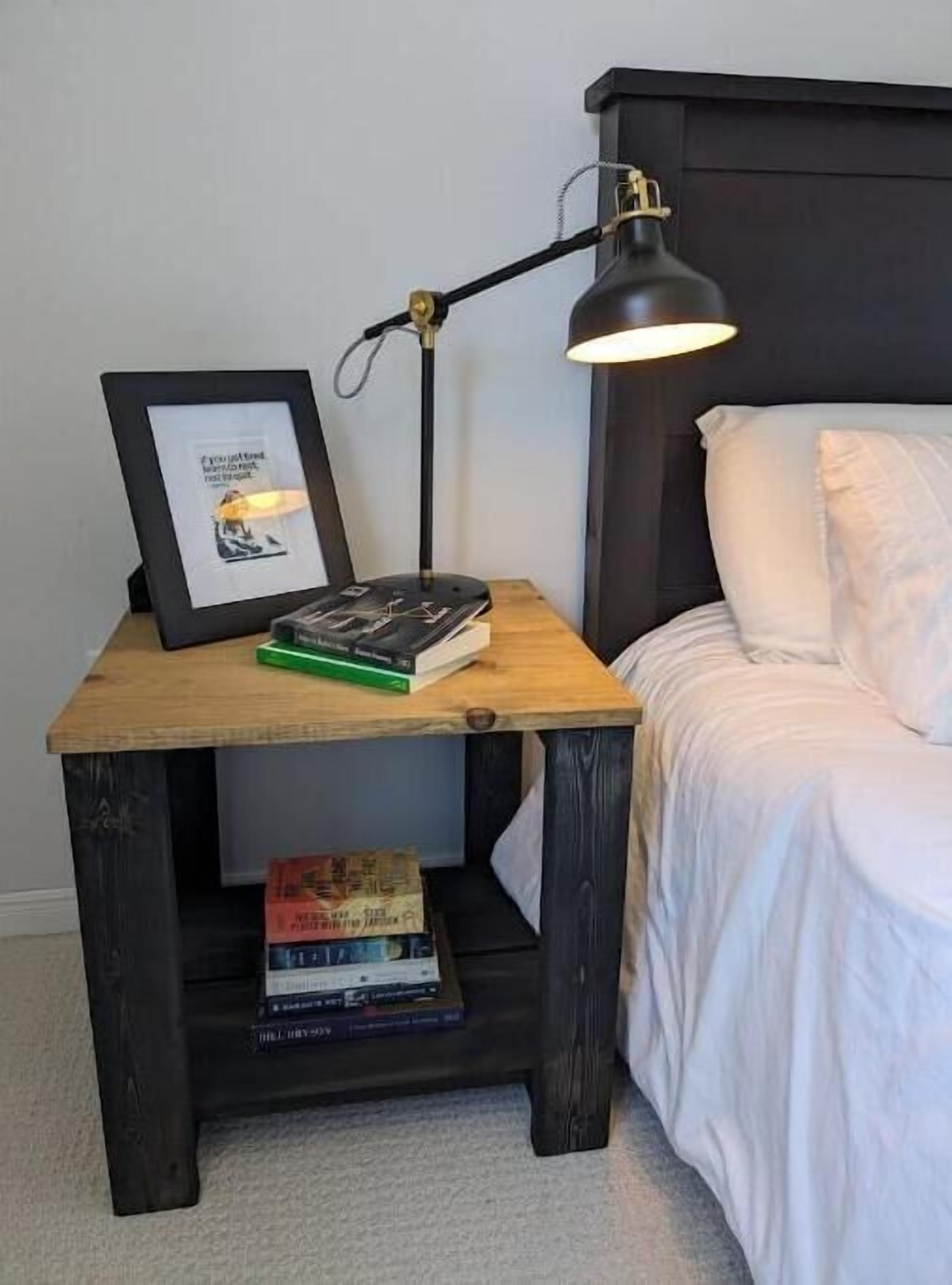 A small bedside table with a framed picture, a lamp, and books.