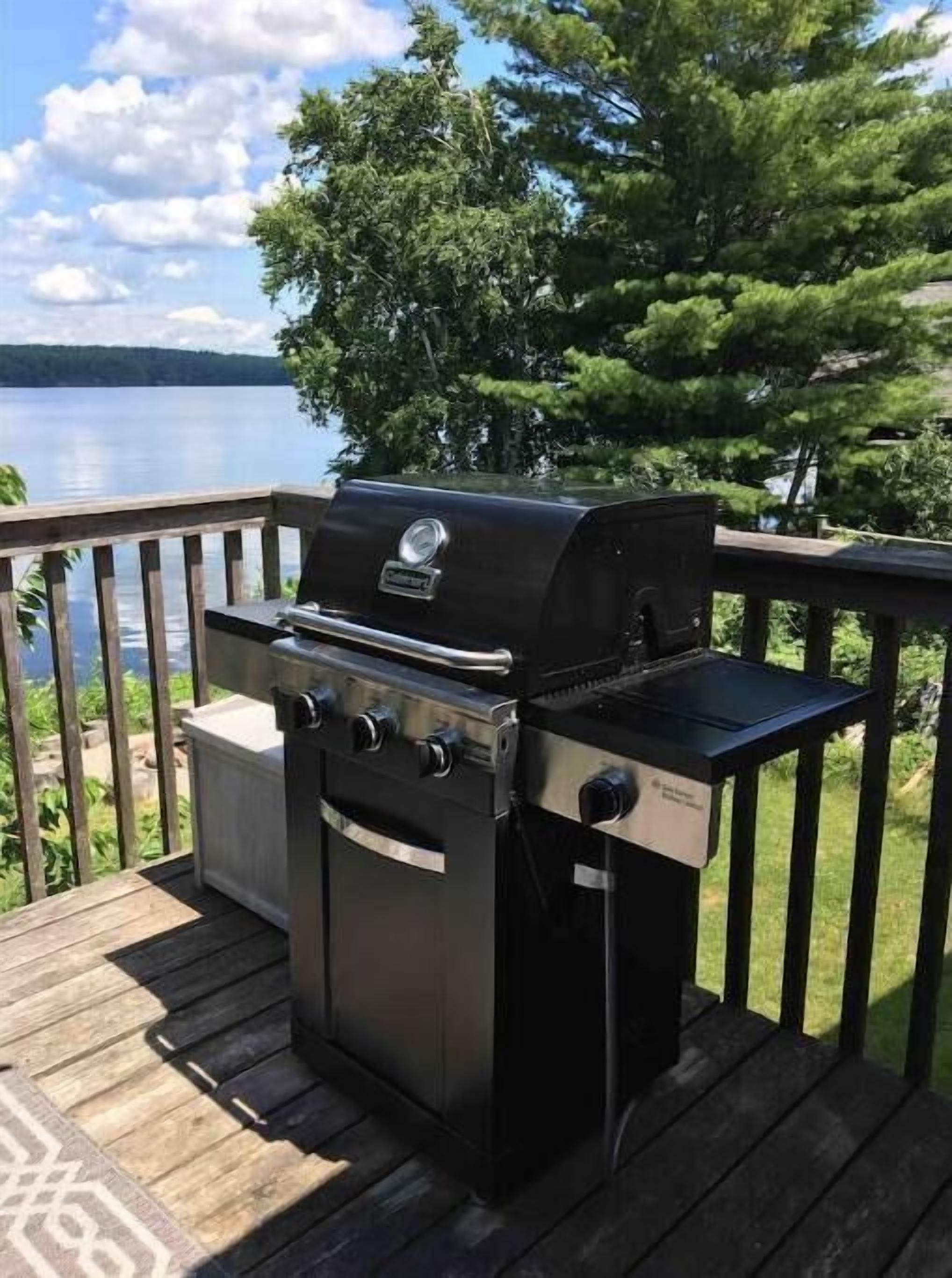 A barbecue grill on a wooden deck with a lake view.