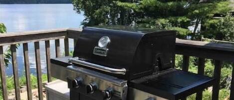 A barbecue grill on a wooden deck with a lake view.