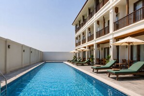 Una piscina con sillas de descanso y sombrillas, rodeada por un edificio con balcones.