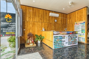 A reception area with a wooden wall, a reception desk, a clock, and a wall-mounted menu board. - Vang Vieng Charming Boutique Hotel (Vang Vieng)