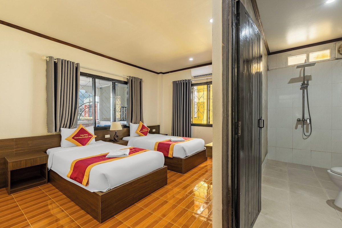 A hotel room with two beds, a shower, and a view of the outside.