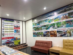 A reception area with a bus ticket poster, a train ticket poster, and a wall with pictures of tourist attractions.