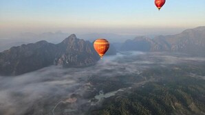 Een luchtballon boven een bergachtig landschap met een rivier en beboste gebieden.