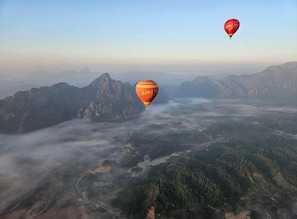 A hot air balloon over a mountainous landscape with a river and forested areas. - Vang Vieng Charming Boutique Hotel (Vang Vieng)