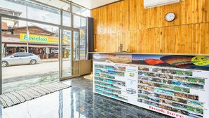 Een hotel receptie met een houten wand, een klok en een glazen deur die naar buiten leidt.