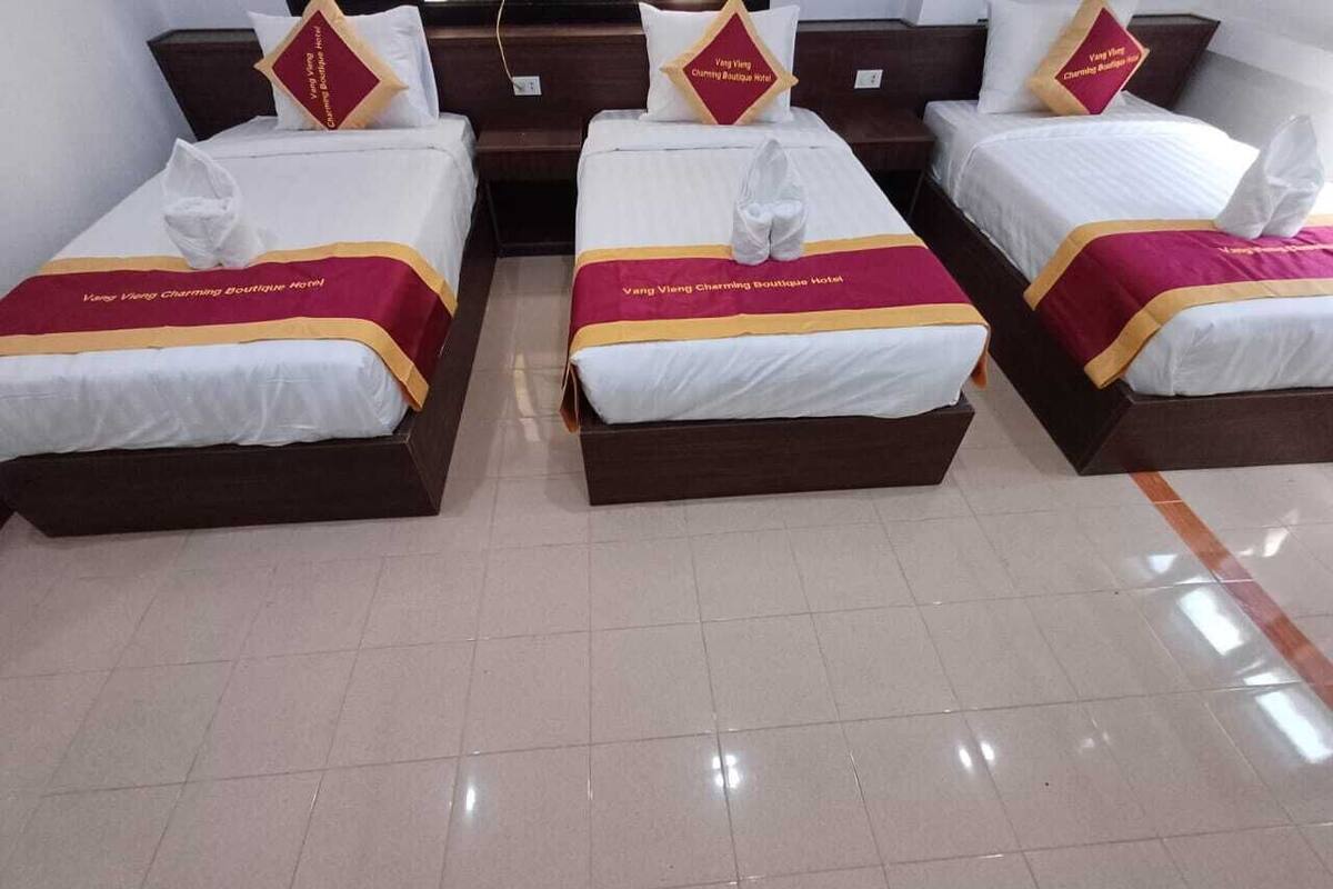 A hotel room with three beds, each with a white and maroon bedspread and matching pillows.