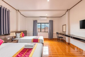 Ein Hotelzimmer mit zwei Betten, einem Schreibtisch, einem Stuhl, einem Fernseher und einem Fenster mit Vorhängen.