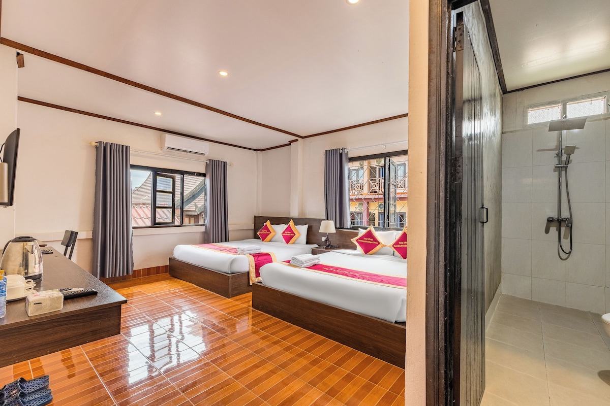 A hotel room with two beds, a desk with a kettle, and a shower area.