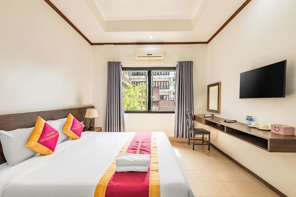 A hotel room with a bed, a desk, a chair, a TV, and a window with curtains.