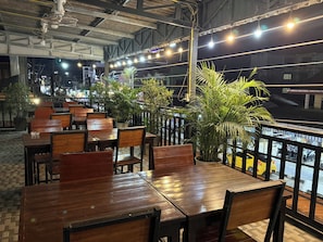 An outdoor seating area with wooden tables and chairs, potted plants, and a view of the street. - Vang Vieng Charming Boutique Hotel (Vang Vieng)