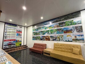 A lobby with a reception desk, a brown sofa, and a wall displaying various tour services. - Vang Vieng Charming Boutique Hotel (Vang Vieng)