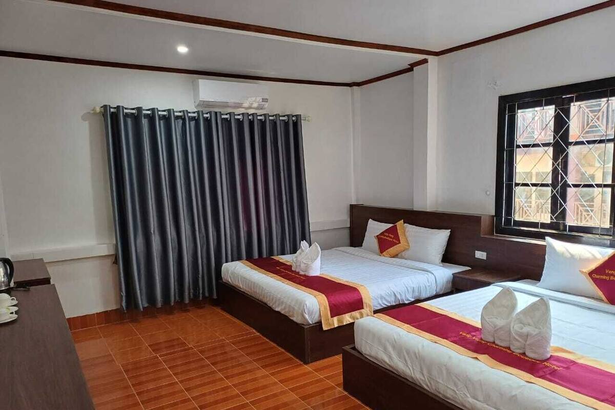 A hotel room with two beds, a wooden floor, a window with a view, and a curtain.