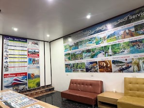 A reception area with a bus ticket poster, a train ticket poster, and a wall with pictures of tourist attractions. - Vang Vieng Charming Boutique Hotel (Vang Vieng)