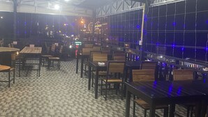 An indoor restaurant with a patterned floor, wooden tables and chairs, and string lights.