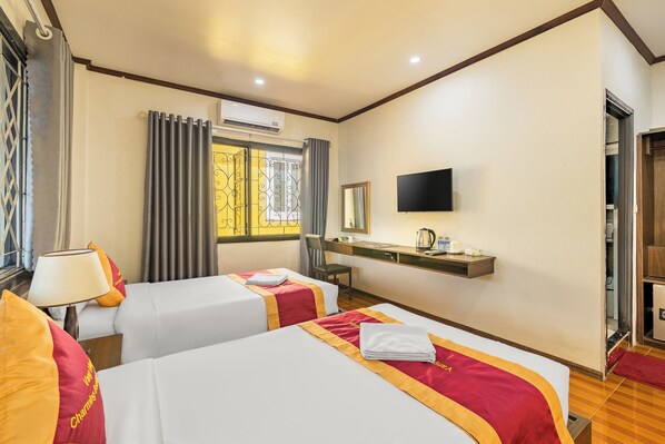 A hotel room with two beds, a television, a desk with a mirror, and an air conditioning unit.