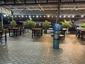 An outdoor patio area with multiple tables and chairs, surrounded by potted plants.