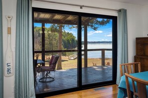 A room with a large sliding glass door leading to an outdoor deck with a view of a lake and trees.