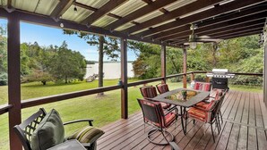 A covered outdoor patio with a table and chairs, a grill, and a view of a lake. - Kate's Kayak Cove on Lake Keowee! (Seneca)