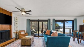 A living room with a sofa, coffee table, and fireplace. There is a large window with a view of the outdoors. - Kate's Kayak Cove on Lake Keowee! (Seneca)