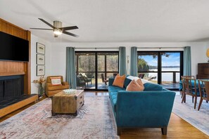 A living room with a sofa, coffee table, and fireplace. There is a large window with a view of the outdoors.