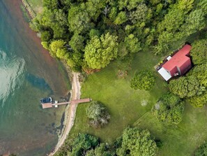 An aerial view of a property with a red-roofed building, a dock, and a grassy area with trees. - Kate's Kayak Cove on Lake Keowee! (Seneca)