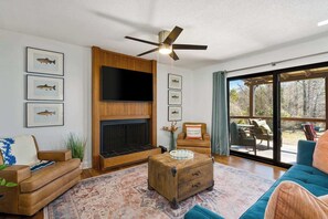 Un salon doté d’une cheminée, d’un ventilateur de plafond et d’une grande fenêtre donnant sur l’extérieur.