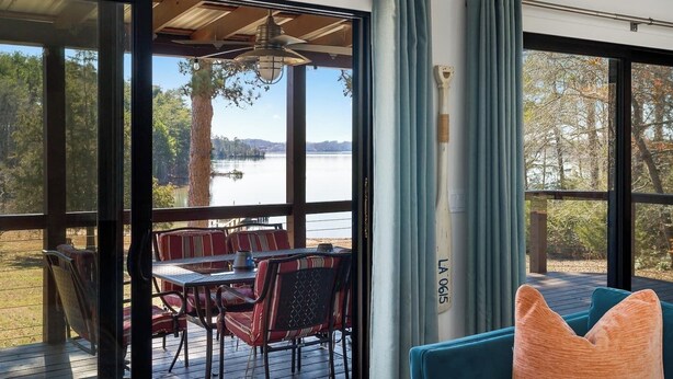 A room with large windows, a dining table with chairs, and a view of a lake. - Kate's Kayak Cove on Lake Keowee! (Seneca)