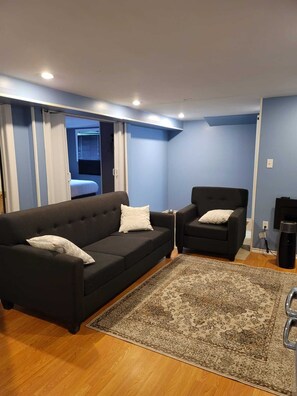 Una sala de estar con un sofá negro, un sillón negro y una alfombra estampada.