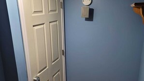 A hallway with a white door, a blue wall, a wooden floor, and a small mat at the entrance.