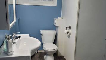 Un baño con lavamanos, inodoro y ventana con cortinas de encaje.
