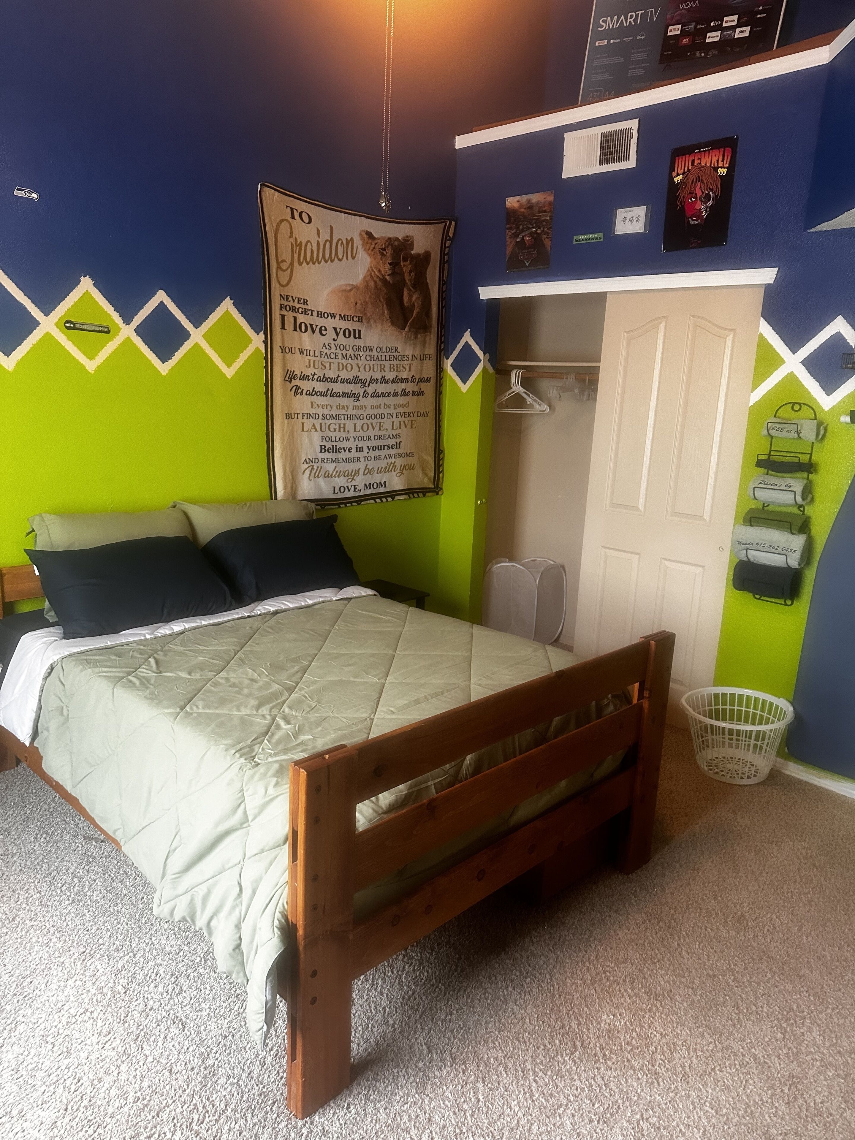 Ein Schlafzimmer mit Bett, Kissen, einem Holzkopfende, einem weißen Kleiderschrank, einer Wand mit einem Poster und einem kleinen weißen Korb.