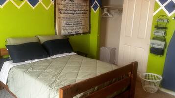 Ein Schlafzimmer mit Bett, Kissen, einem Holzkopfende, einem weißen Kleiderschrank, einer Wand mit einem Poster und einem kleinen weißen Korb.