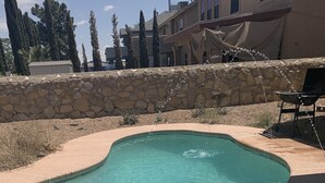 A swimming pool with a stone wall and a pergola with string lights. - B&B at the Paseo's by Wanda (El Paso)