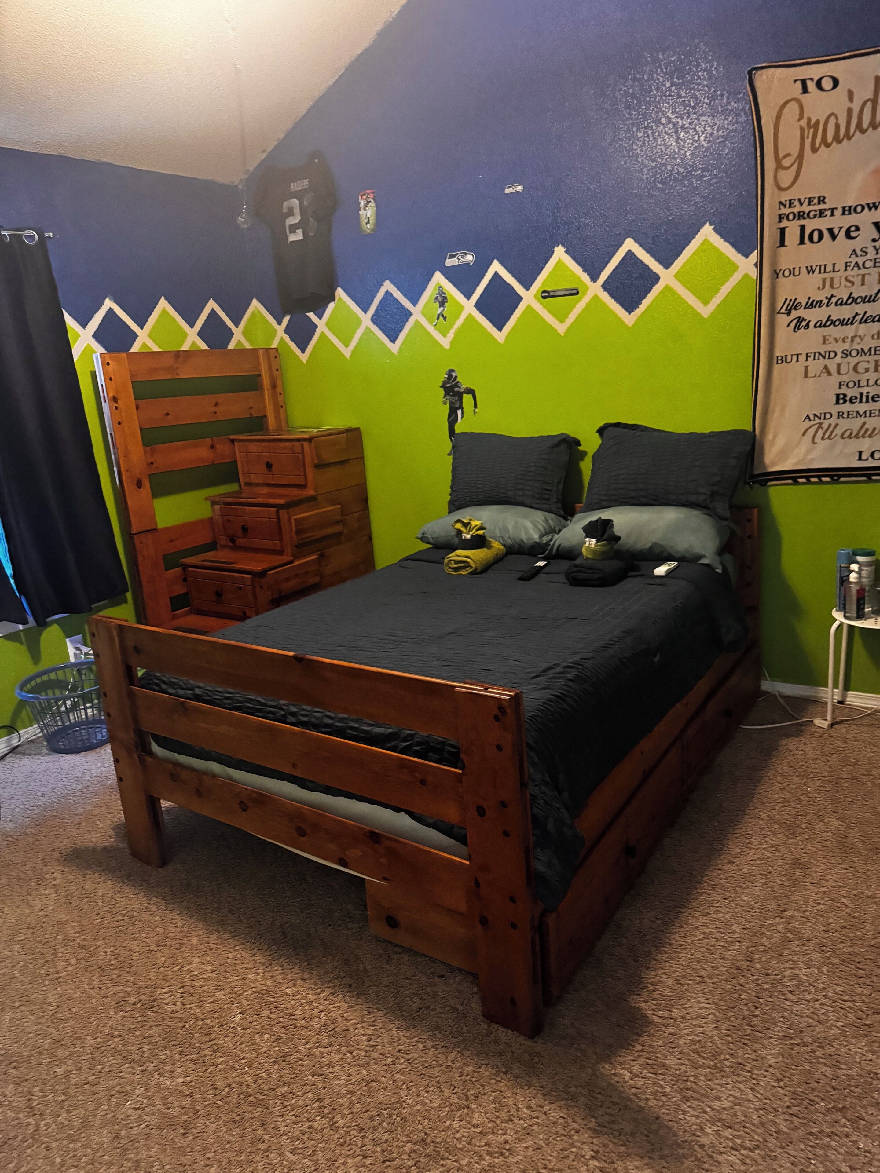 A bedroom with a wooden bed, a dresser, a wall with a geometric pattern, and a motivational poster.