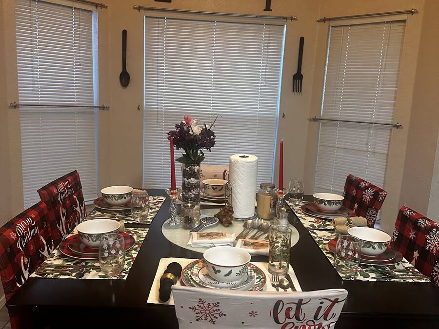 A dining room with a Christmas theme, featuring a long table set for four, flanked by chairs with festive upholstery.