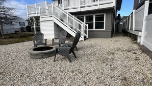 Ein zweistöckiges Haus mit weißer Fassade, einer überdachten Terrasse mit Feuerstelle und einer Treppe, die zu einem Balkon führt.