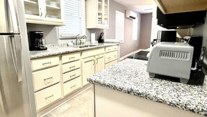 Eine Küche mit weißen Schränken, einer Granit Arbeitsplatte, einem Kühlschrank, einer Kaffeemaschine und einer Mikrowelle.