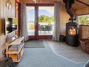 Een gezellig interieur van een chalet met een televisie, een houten bank, een open haard en uitzicht op de omgeving.