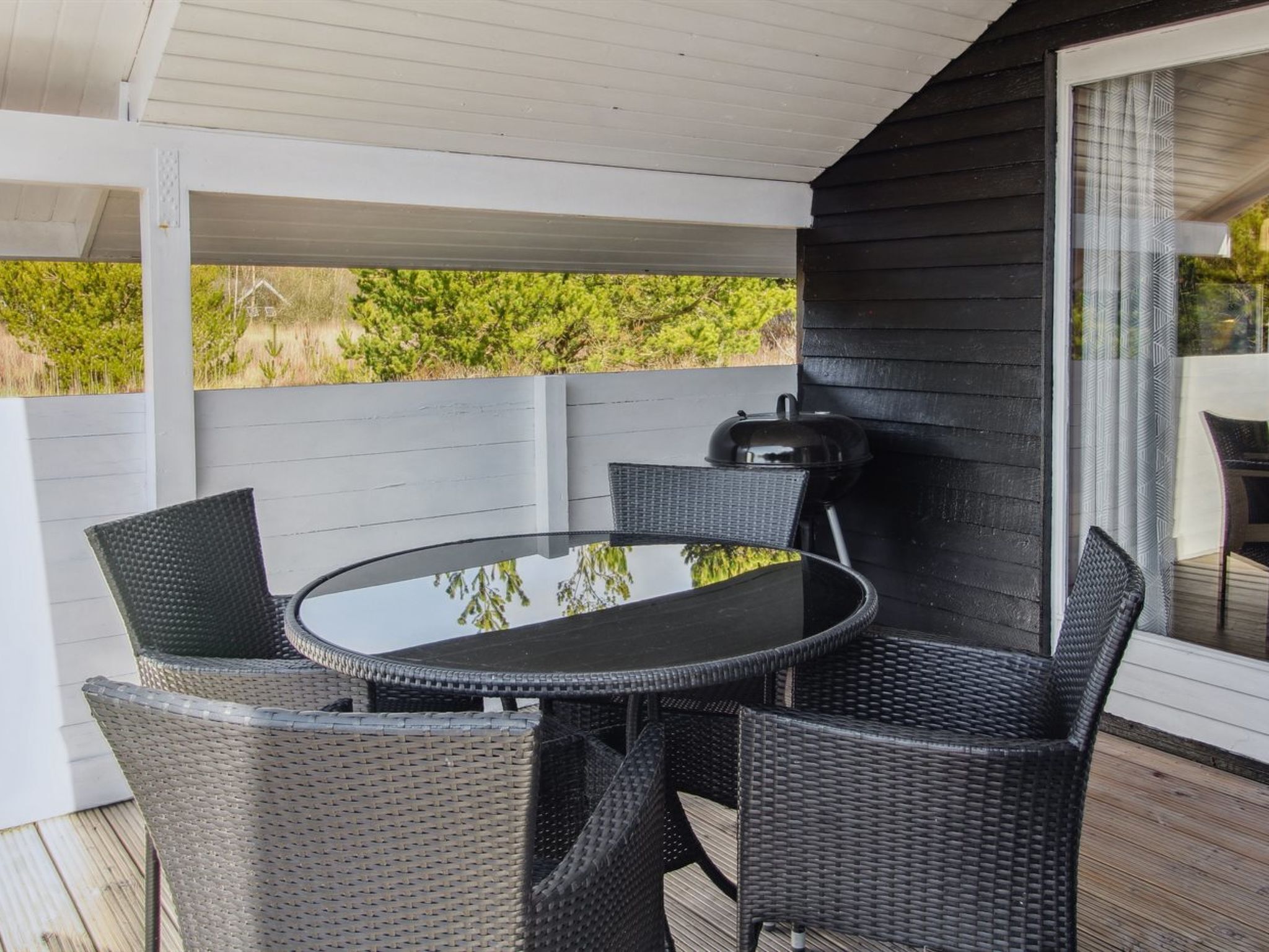 Un espacio al aire libre cubierto con una mesa redonda y cuatro sillas, una parrilla y un vidrio que da a una terraza.