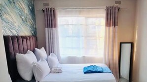 Una habitación de hotel con una cama, una mesita de noche, un espejo y una ventana con cortinas.