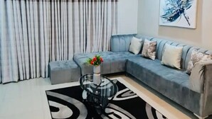 Una sala de estar con un sofá gris, una mesa de centro de vidrio con un jarrón de flores y una alfombra estampada en blanco y negro.
