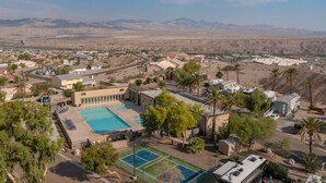 A residential area with a large swimming pool, tennis courts, and a view of distant mountains. - Stylish Oasis Tiny Home Pool Hot Tub Pickleball Bullhead City 10 min to Laughlin (Bullhead City)