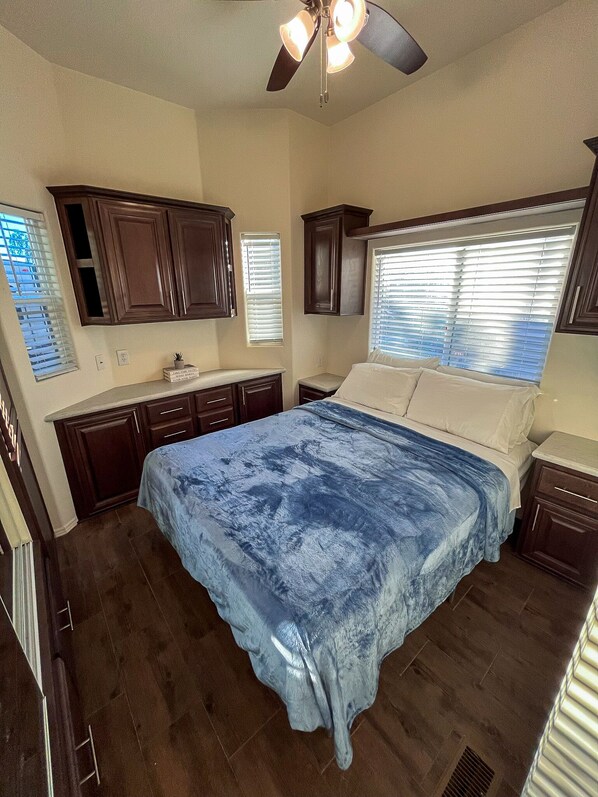 A bedroom with a bed, wooden cabinets, a ceiling fan, and a window with blinds.