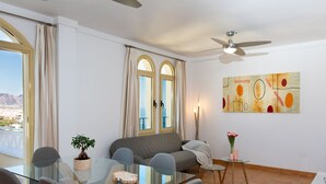 Un salon moderne avec une table à manger en verre, un canapé gris et un ventilateur de plafond.