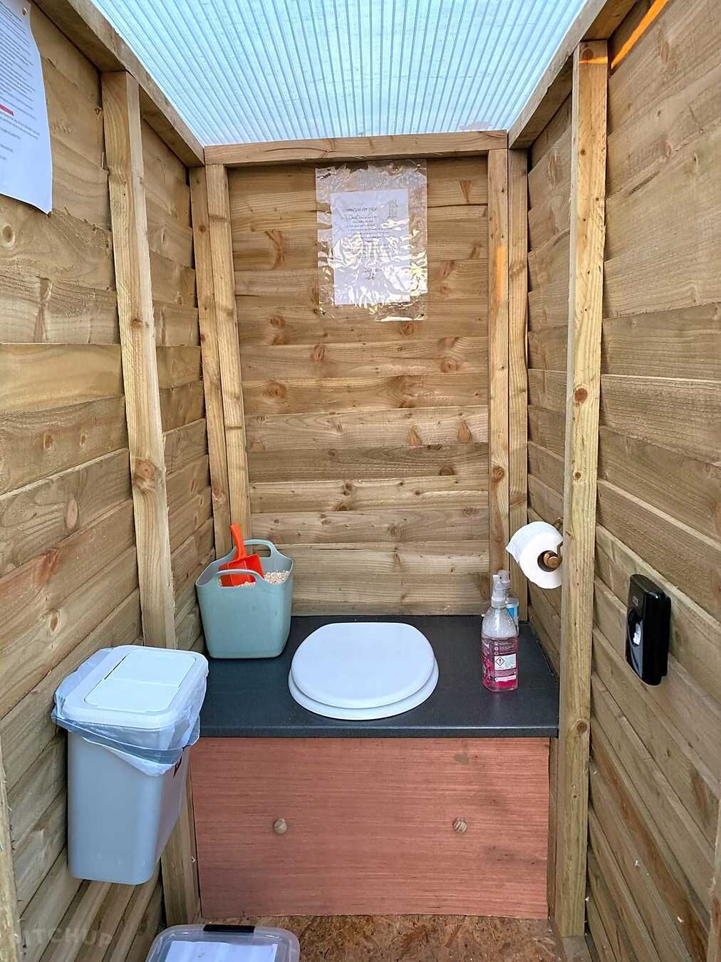 Une petite salle de bain en bois comprenant des toilettes, un lavabo et une poubelle.